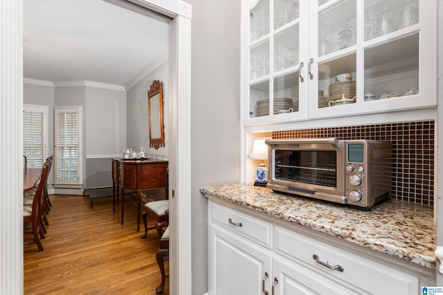 bar featuring white cabinetry, ornamental molding, light stone counters, and light hardwood / wood-style flooring