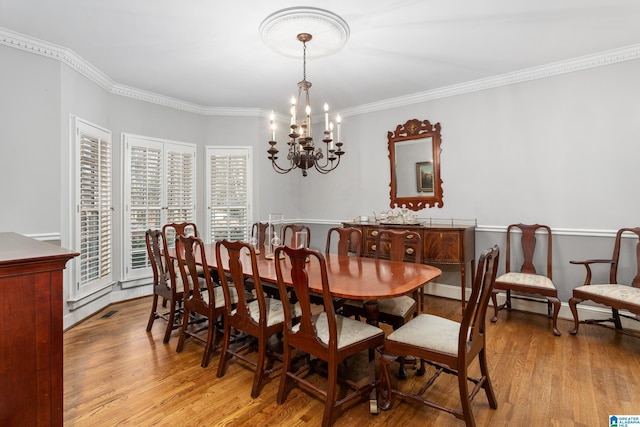 dining space with light wood-type flooring, an inviting chandelier, and crown molding