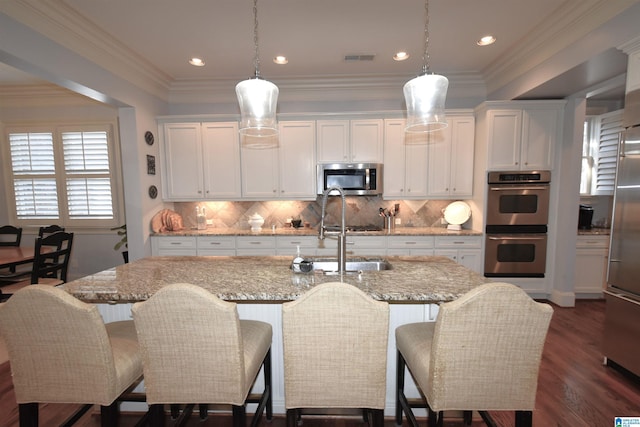 kitchen featuring light stone countertops, pendant lighting, stainless steel appliances, an island with sink, and white cabinetry