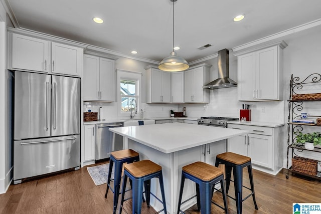 kitchen featuring stainless steel appliances, crown molding, a breakfast bar, a kitchen island, and wall chimney range hood