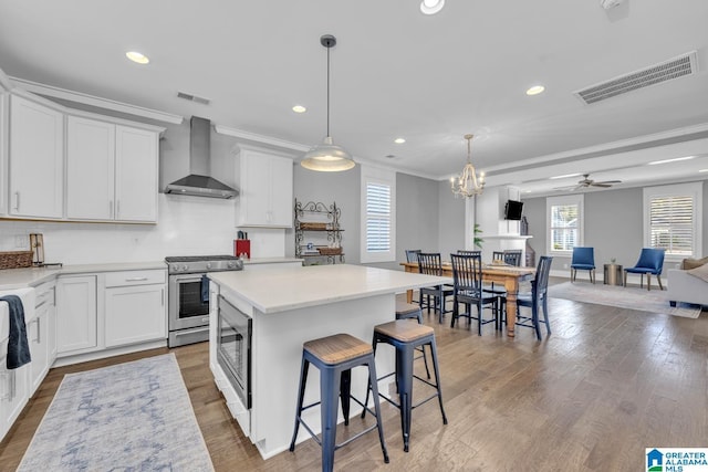 kitchen with decorative light fixtures, white cabinets, a kitchen island, wall chimney range hood, and appliances with stainless steel finishes