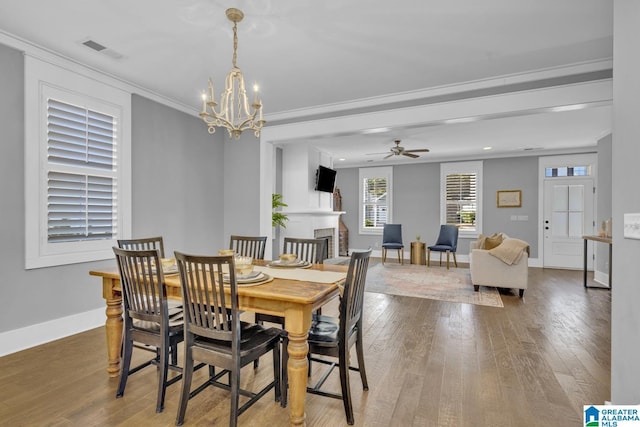 dining space featuring a large fireplace, ceiling fan with notable chandelier, ornamental molding, and hardwood / wood-style floors