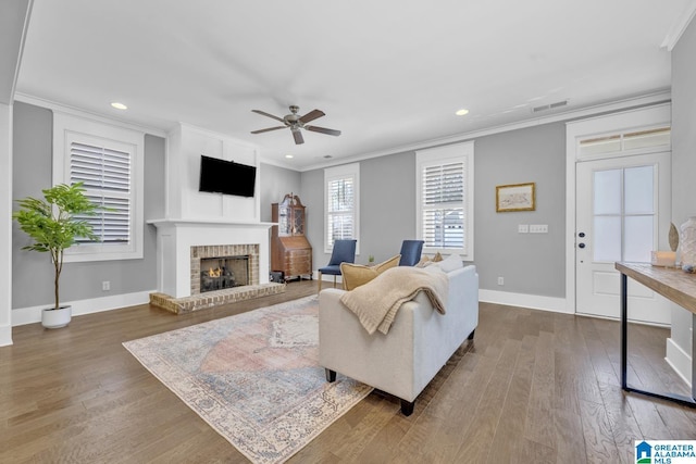 living room with ornamental molding, ceiling fan, dark hardwood / wood-style flooring, and a brick fireplace