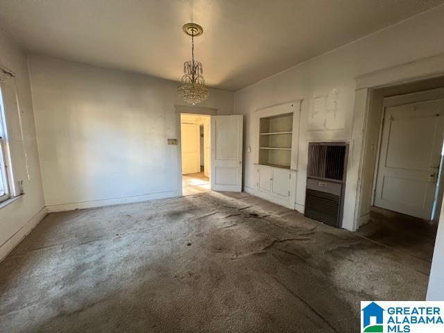 unfurnished living room featuring carpet floors, built in features, and a notable chandelier