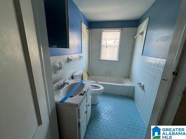 full bathroom featuring tiled shower / bath, tile patterned flooring, vanity, tile walls, and toilet