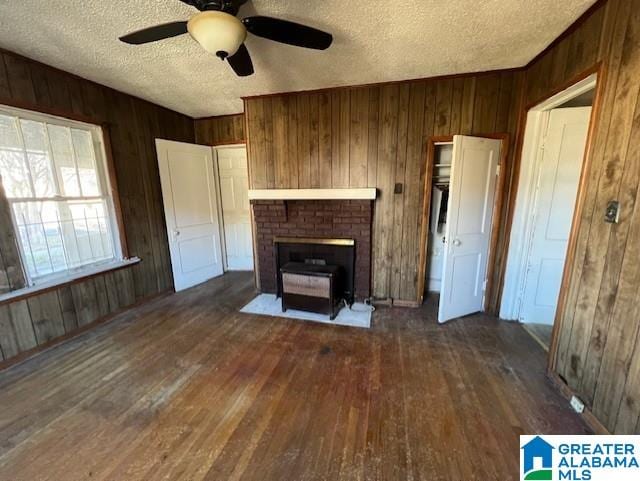 unfurnished living room featuring ceiling fan, dark wood-type flooring, wood walls, and a textured ceiling