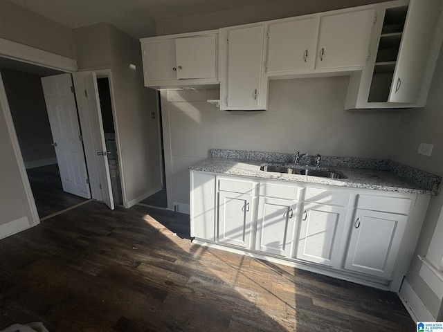 kitchen featuring white cabinets, dark wood-type flooring, light stone counters, and sink