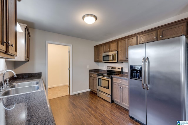 kitchen featuring appliances with stainless steel finishes, dark stone countertops, dark hardwood / wood-style flooring, and sink