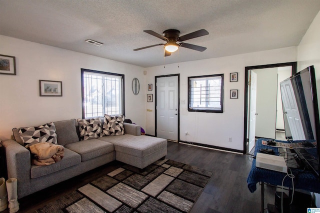 living room featuring a textured ceiling, dark wood-type flooring, plenty of natural light, and ceiling fan