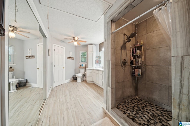 bathroom featuring a textured ceiling, ceiling fan, toilet, walk in shower, and vanity