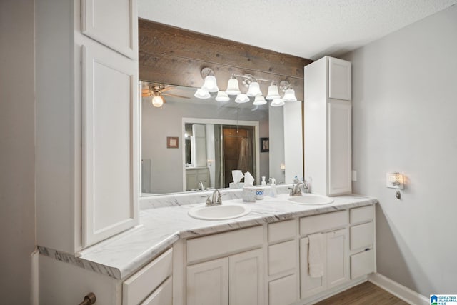 bathroom with a textured ceiling, ceiling fan, wood-type flooring, and vanity