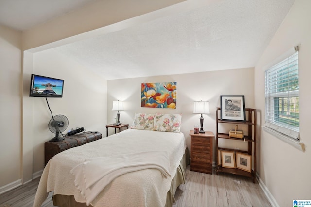 bedroom with a textured ceiling, light wood-type flooring, and lofted ceiling