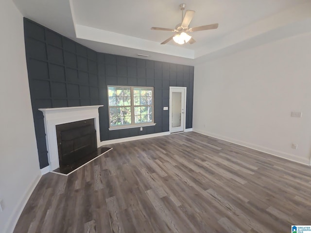 unfurnished living room with ceiling fan, a tray ceiling, and wood-type flooring