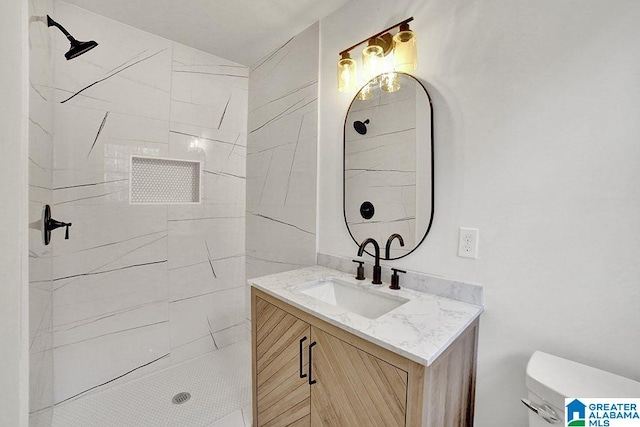 bathroom with toilet, a tile shower, and vanity