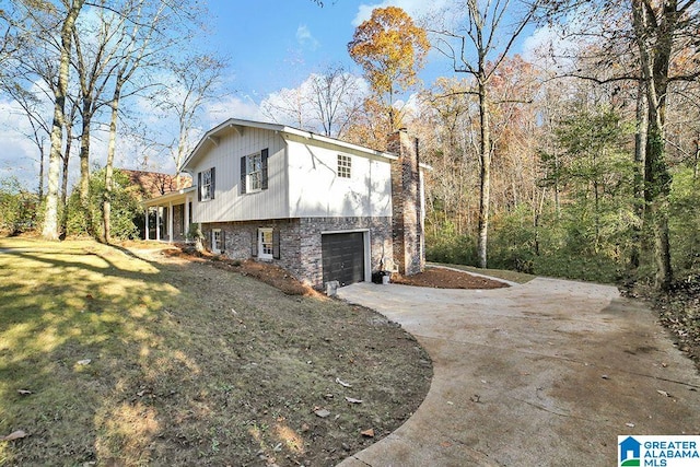 view of side of property featuring concrete driveway, a yard, a chimney, and an attached garage