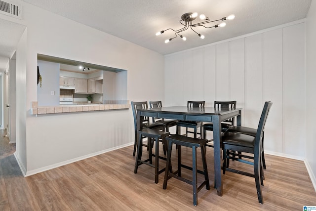 dining room with a textured ceiling, a chandelier, and light hardwood / wood-style floors