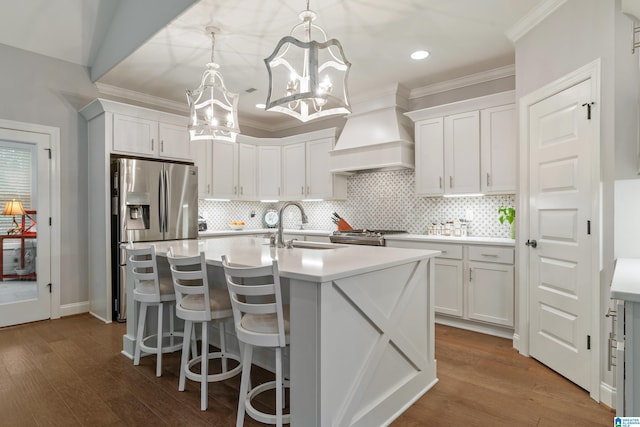 kitchen with pendant lighting, white cabinets, stainless steel appliances, a kitchen island with sink, and custom range hood