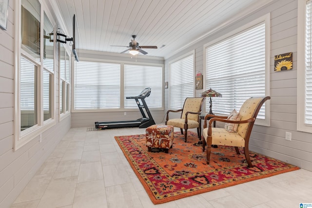 living area with ceiling fan, wood walls, crown molding, and wooden ceiling