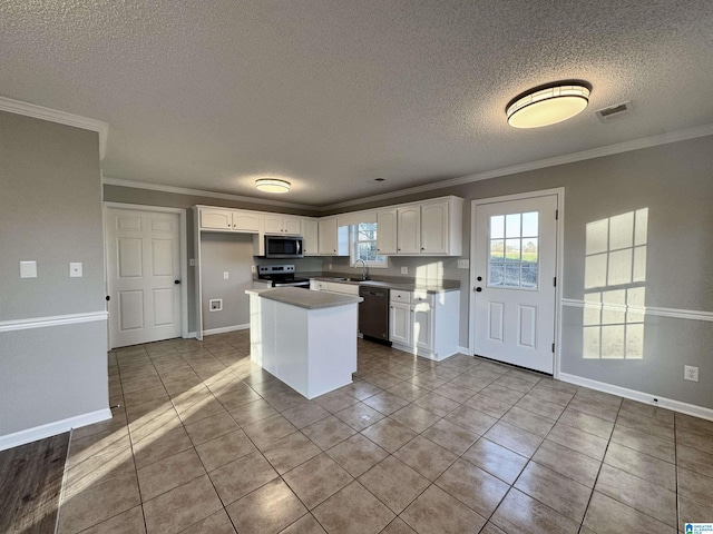 kitchen with stainless steel appliances, light tile patterned floors, a kitchen island, crown molding, and white cabinetry