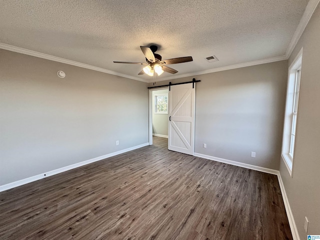 unfurnished bedroom with a textured ceiling, ceiling fan, a barn door, multiple windows, and dark wood-type flooring