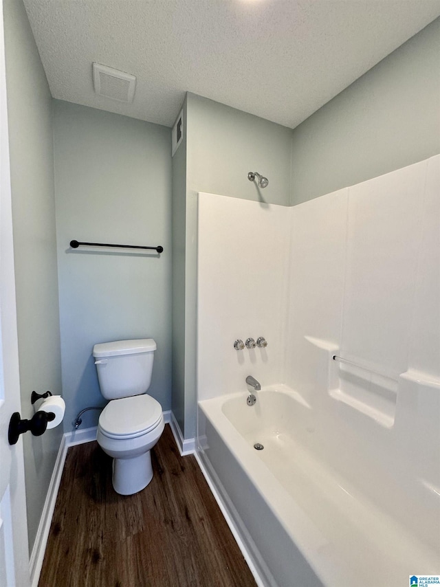 bathroom with toilet, wood-type flooring, a textured ceiling, and bathing tub / shower combination