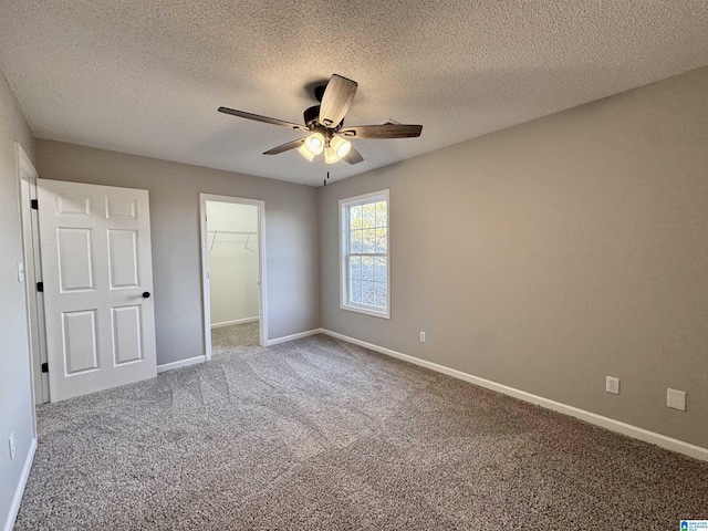 unfurnished bedroom with a textured ceiling, carpet, ceiling fan, a closet, and a walk in closet