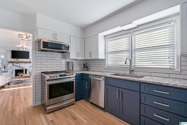 kitchen with stainless steel appliances, blue cabinetry, white cabinetry, a fireplace, and sink