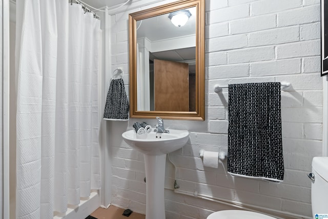 bathroom with toilet, brick wall, and a shower with curtain