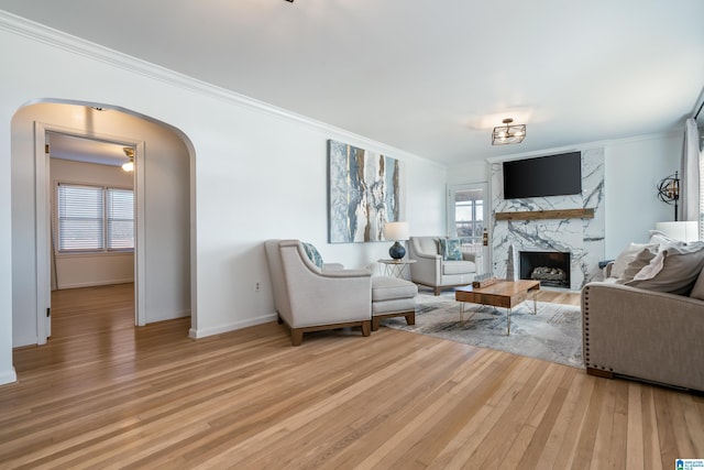 living room featuring a high end fireplace, ornamental molding, a wealth of natural light, and light hardwood / wood-style flooring