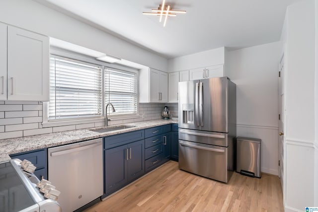 kitchen with appliances with stainless steel finishes, light stone countertops, white cabinets, blue cabinets, and sink