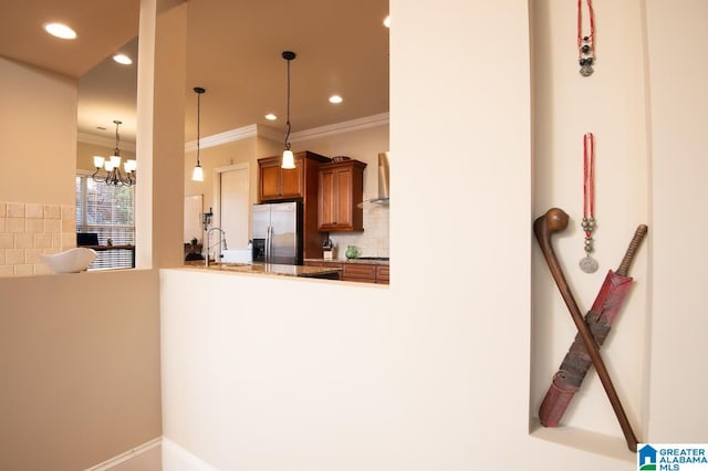 kitchen featuring decorative light fixtures, backsplash, wall chimney range hood, stainless steel refrigerator with ice dispenser, and ornamental molding