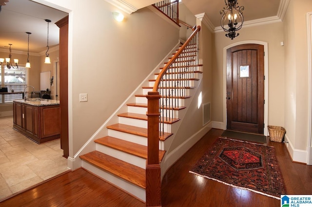 entrance foyer featuring an inviting chandelier, ornamental molding, wood-type flooring, and sink