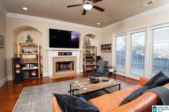 living room with ceiling fan, dark wood-type flooring, a premium fireplace, and ornamental molding