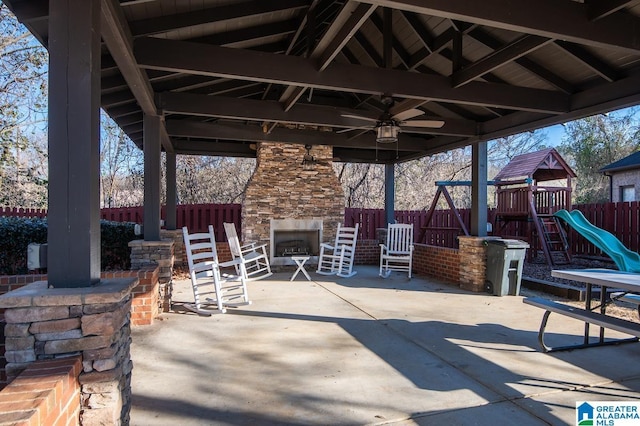 view of patio with a playground and an outdoor stone fireplace