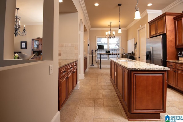 kitchen featuring light stone countertops, pendant lighting, stainless steel refrigerator with ice dispenser, an inviting chandelier, and a center island with sink