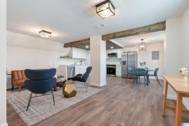 living room featuring electric panel, a notable chandelier, beam ceiling, and light hardwood / wood-style floors