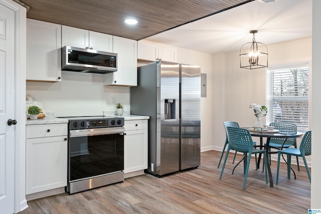 kitchen featuring light wood-type flooring, appliances with stainless steel finishes, hanging light fixtures, and white cabinetry