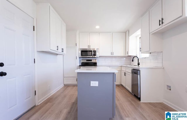 kitchen with stainless steel appliances, light wood-type flooring, a kitchen island, white cabinets, and sink