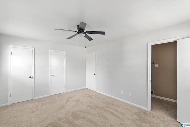 unfurnished bedroom with ceiling fan, light carpet, and multiple closets