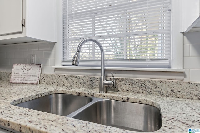 interior details with sink, white cabinetry, backsplash, and light stone countertops