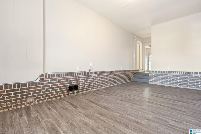 empty room with brick wall and wood-type flooring