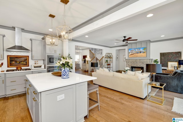 kitchen with pendant lighting, appliances with stainless steel finishes, wall chimney exhaust hood, a kitchen island, and a brick fireplace