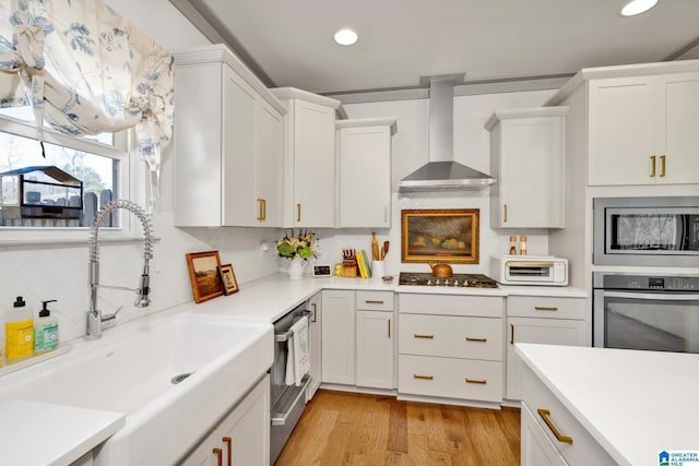 kitchen with sink, wall chimney range hood, stainless steel appliances, and white cabinetry