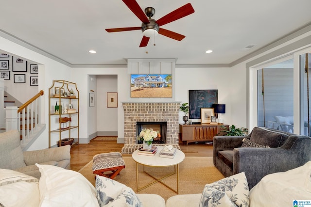 living room with light hardwood / wood-style floors, ornamental molding, ceiling fan, and a fireplace