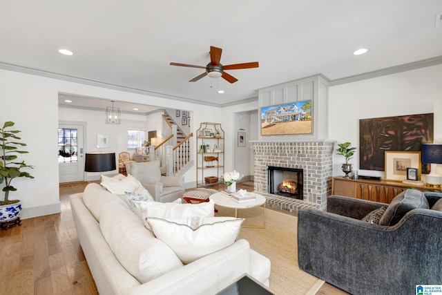 living room featuring a brick fireplace, ornamental molding, hardwood / wood-style flooring, and ceiling fan