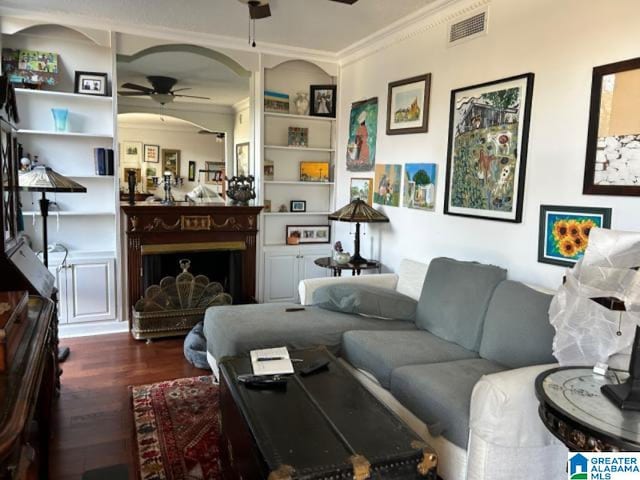 living room featuring ceiling fan, dark wood-type flooring, built in features, and crown molding