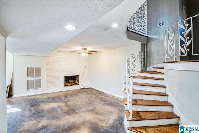 stairway featuring ceiling fan, a fireplace, concrete floors, and a textured ceiling