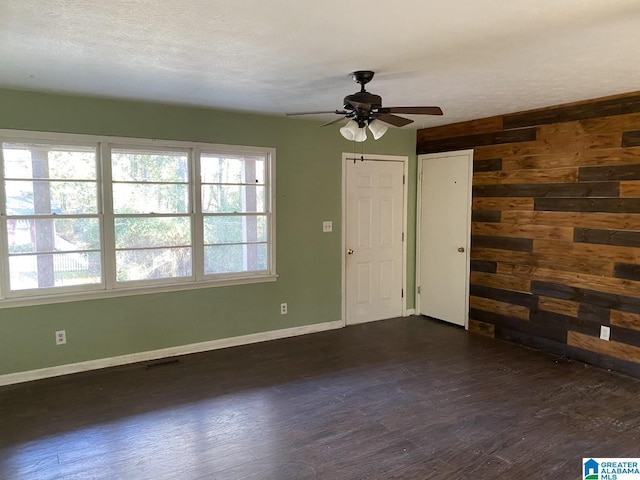 spare room with dark wood-type flooring, ceiling fan, a textured ceiling, and wood walls