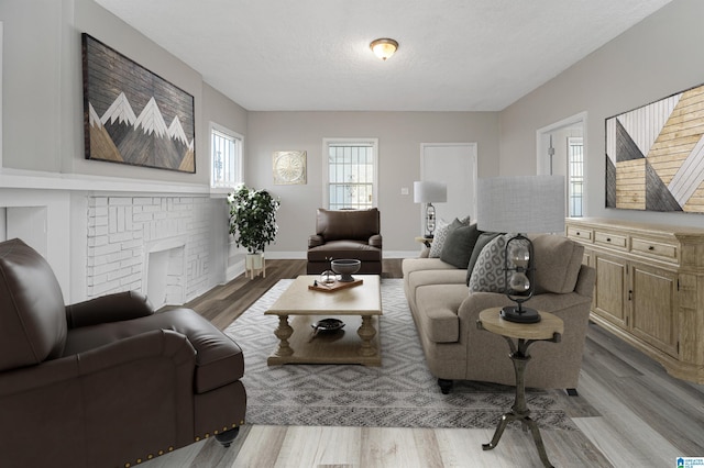 living room with a brick fireplace, a textured ceiling, and light hardwood / wood-style flooring