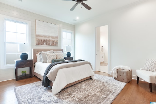 bedroom with ceiling fan, connected bathroom, wood-type flooring, and ornamental molding